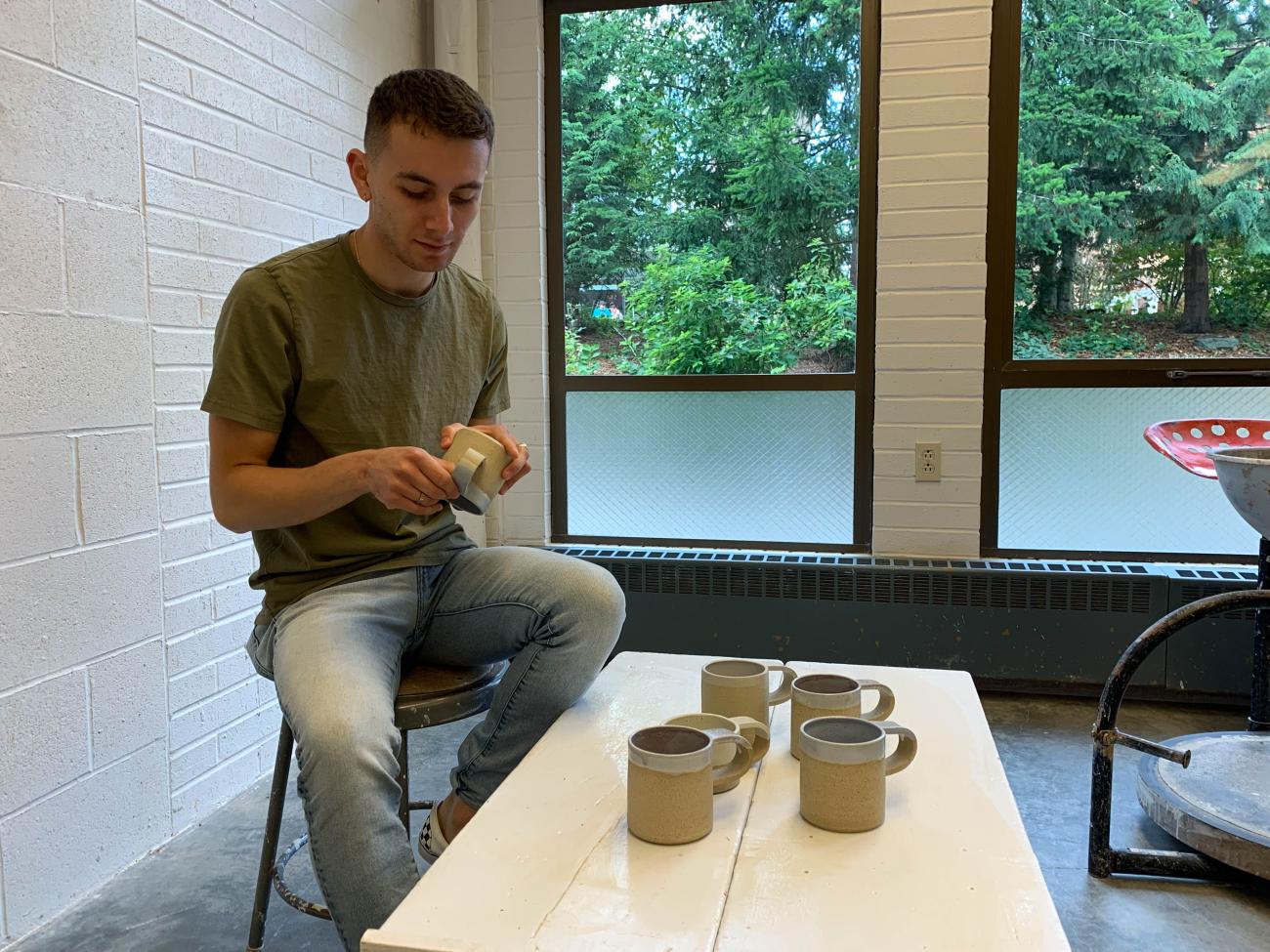 Gabe Virgen sits in the studio and inspects mugs