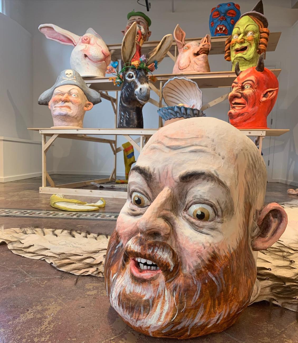 A giant head of Ryan Kelly. Behind are carnivalesque caricatures of animals, demons, witches