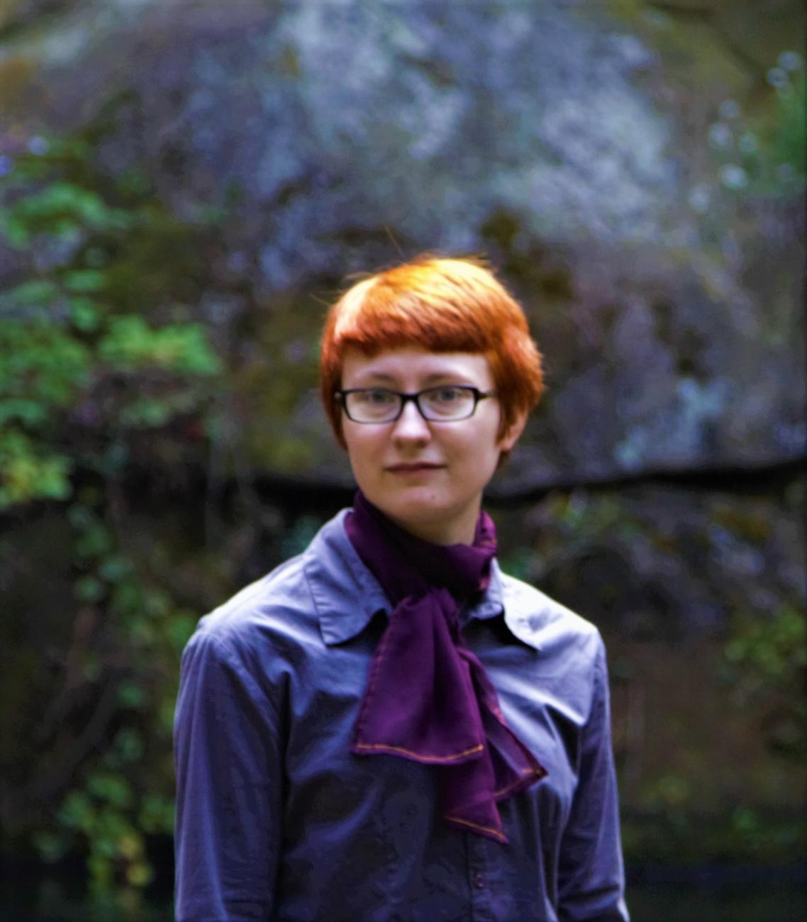 young person with short red hair and a dapper purple shirt and scarf