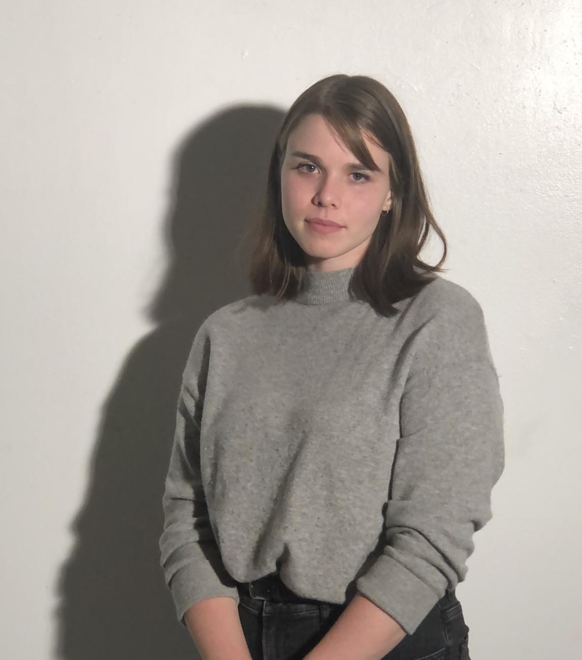 a young person with brown hair and a gray sweater