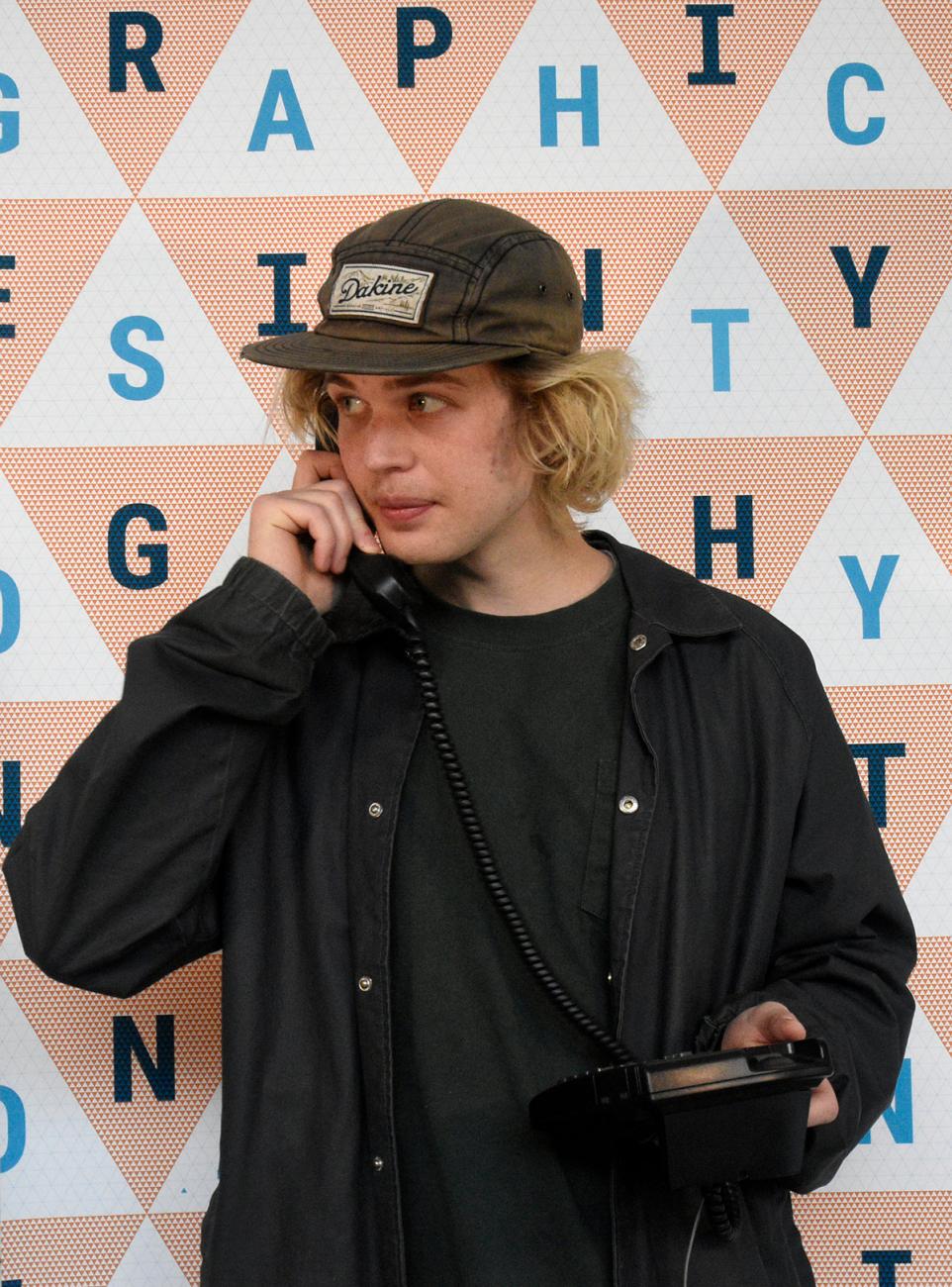 a young person with a black ball cap talks on an older style phone with a corded handset