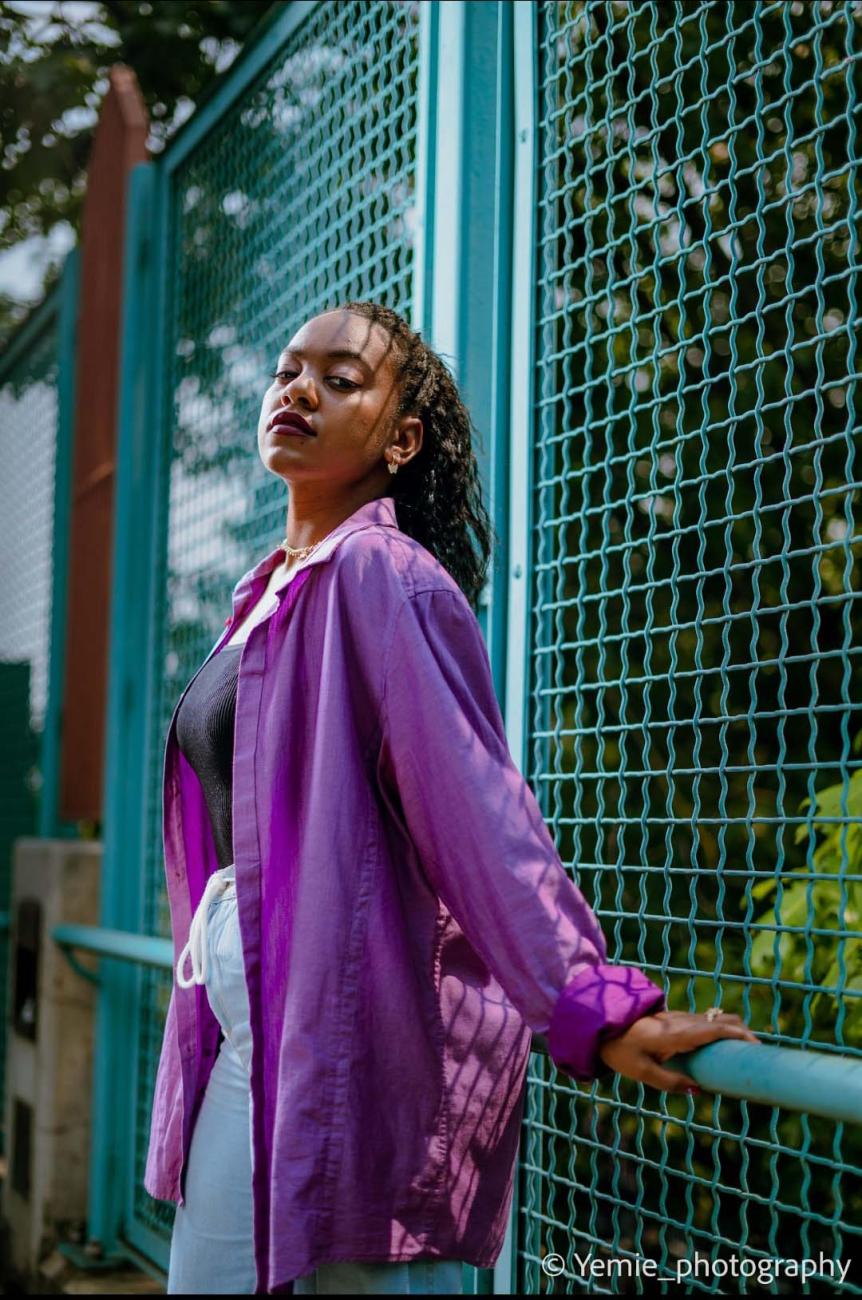 black woman with purple sweater standing against a blue chain link fence