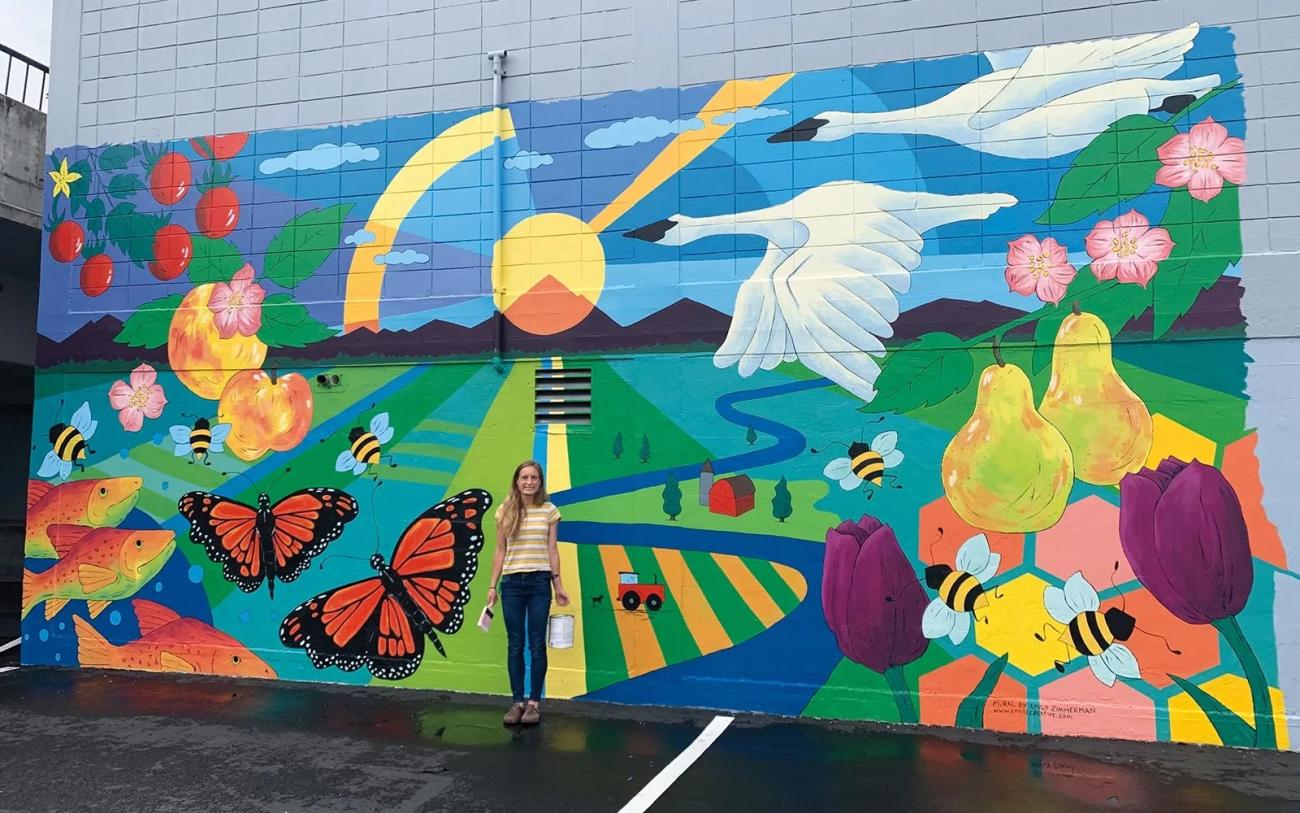 a person stands in front of a very large colorful mural on an exterior building wall