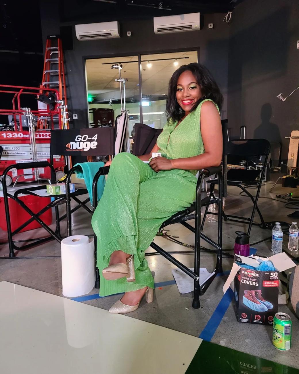 a dancer in a green outfit sits in a director's chair on a video production set