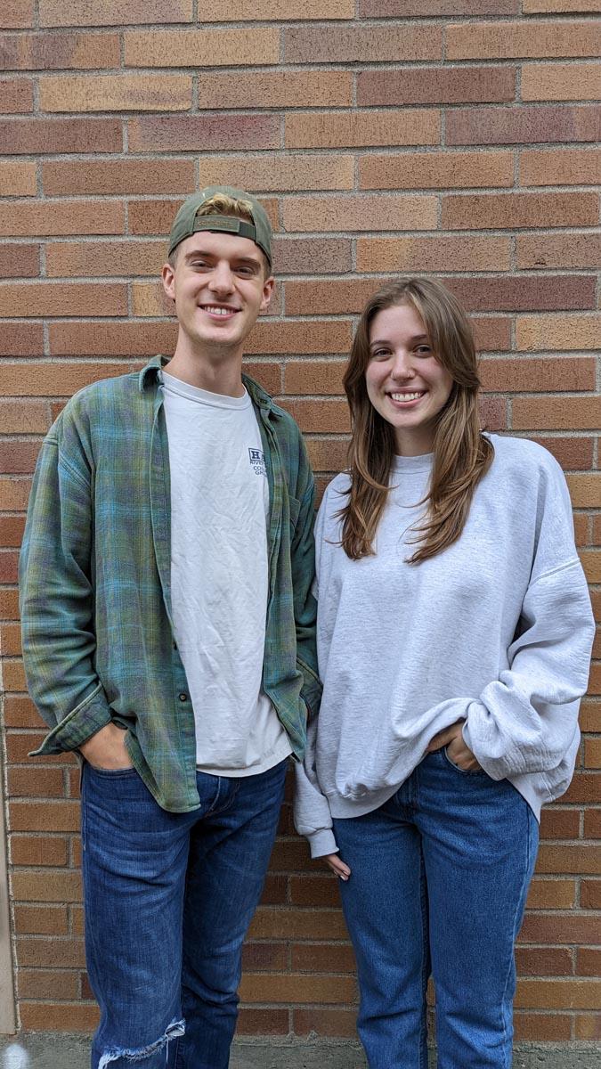 two college students stand in front of a brick wall.