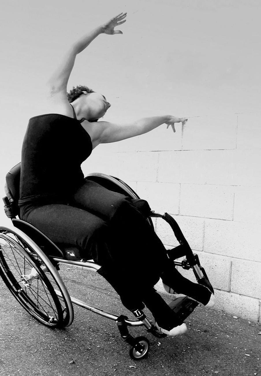 a dancer in a wheelchair leans the chair to the side onto one set of wheels while the dancers arms are extended in the opposite direction in a curve.
