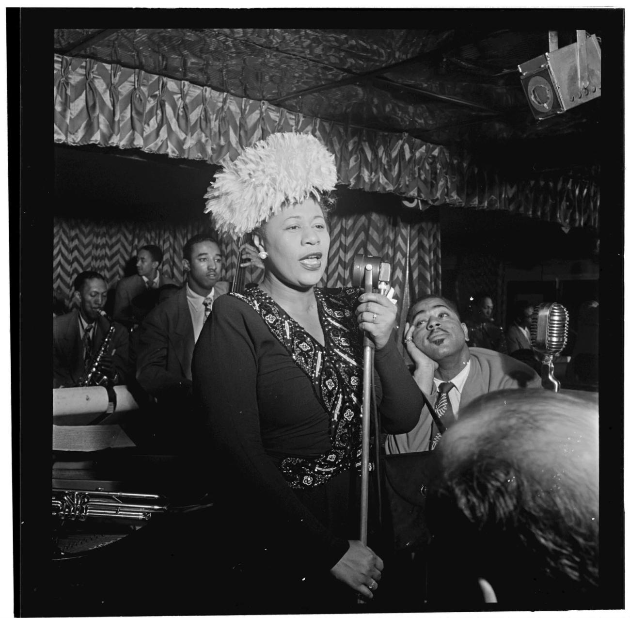 Ella Fiztgerald sings into a microphone in a black and white historical photo