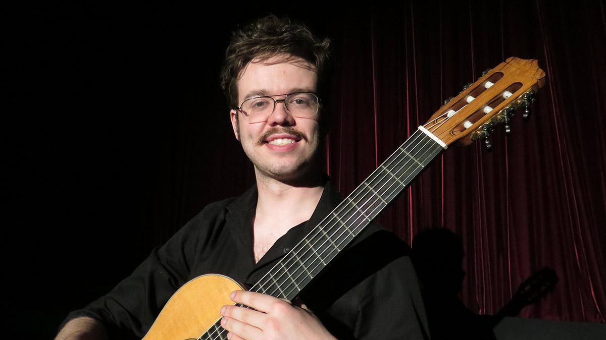Sam Burrows has glasses, a mustache, and a guitar.