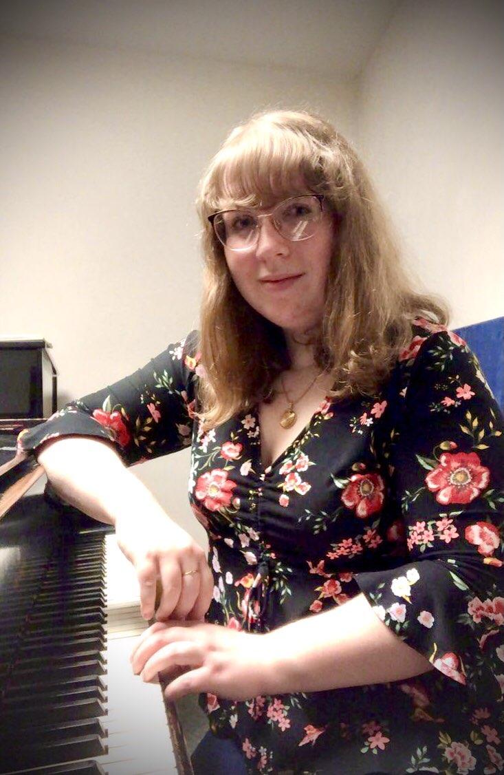 A pianist in a floral print and glasses resting at the keyboard of a piano