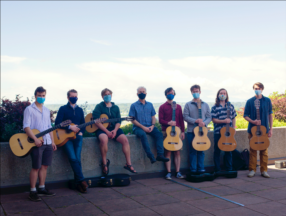 eight guitar players stand near a long planter at the edge of a plaza with watery blue sky behind