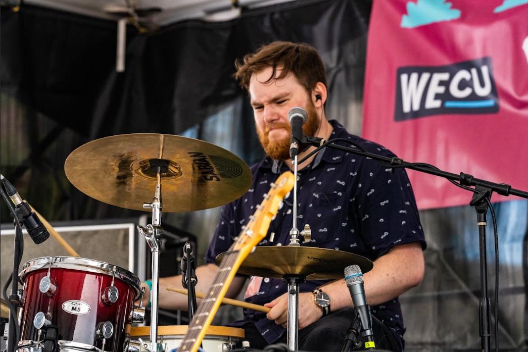 Toby Bruce has a beard and sits behind a drum kit, playing with determination