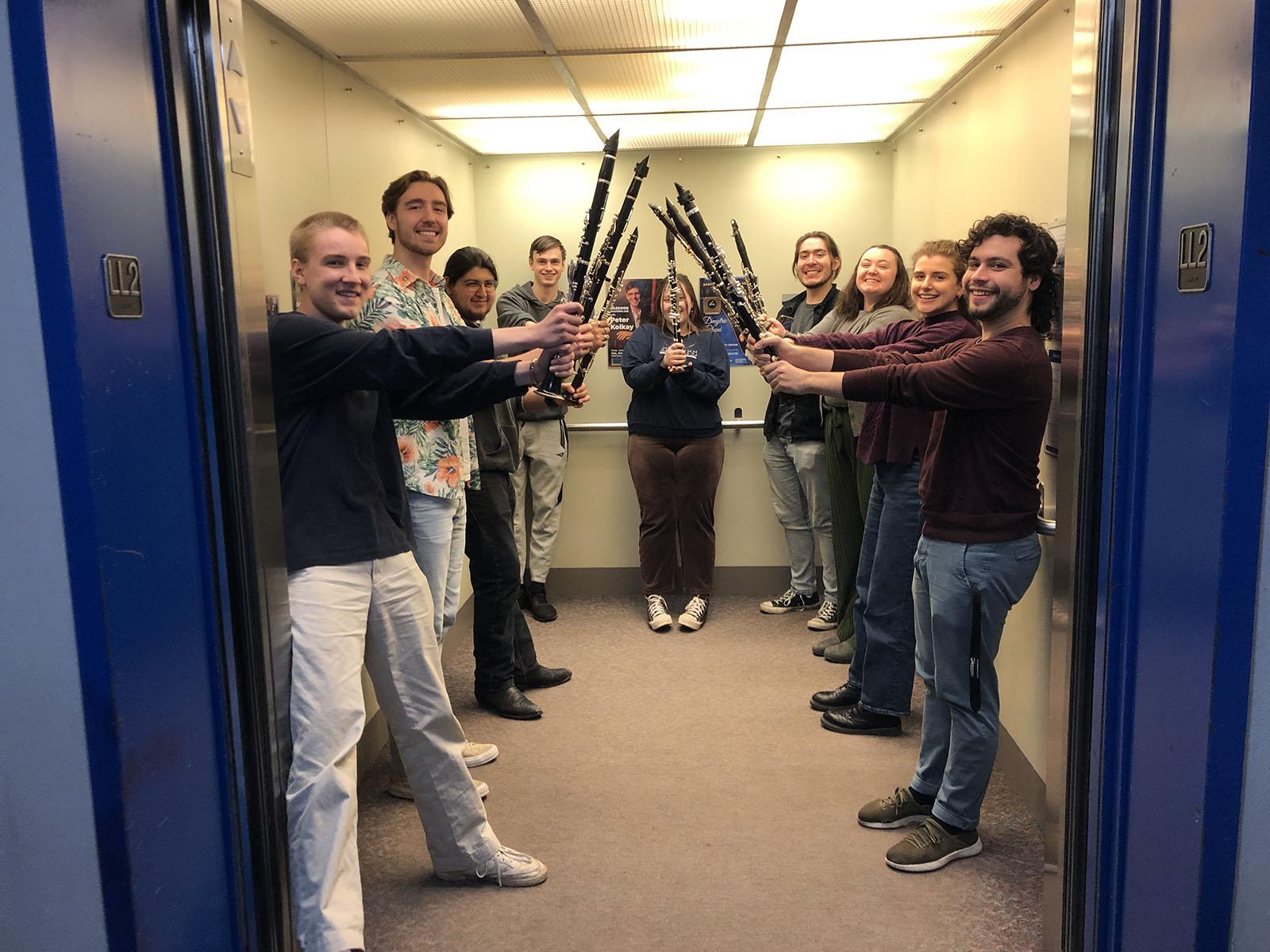 clarinetists line either side of a freight elevator, holding their clarinets aloft, making a tunnel.
