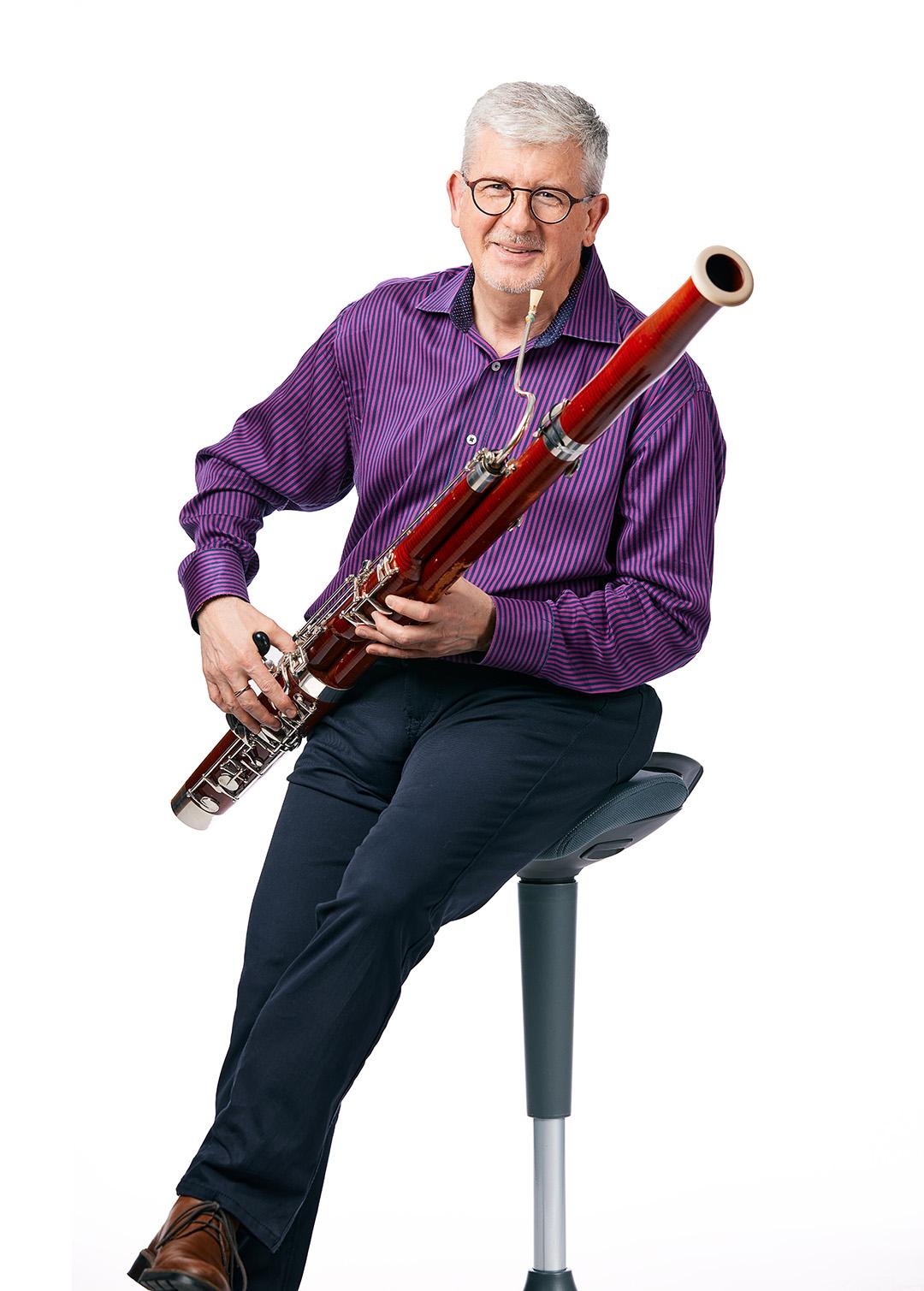 Paul Rafanelli looking friendly and cool, sitting on a stool holding a bassoon