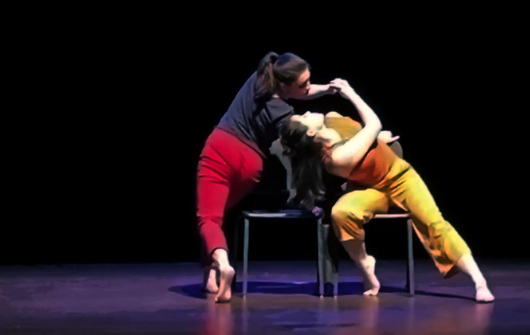 two dancers grip arms and twist around a chair