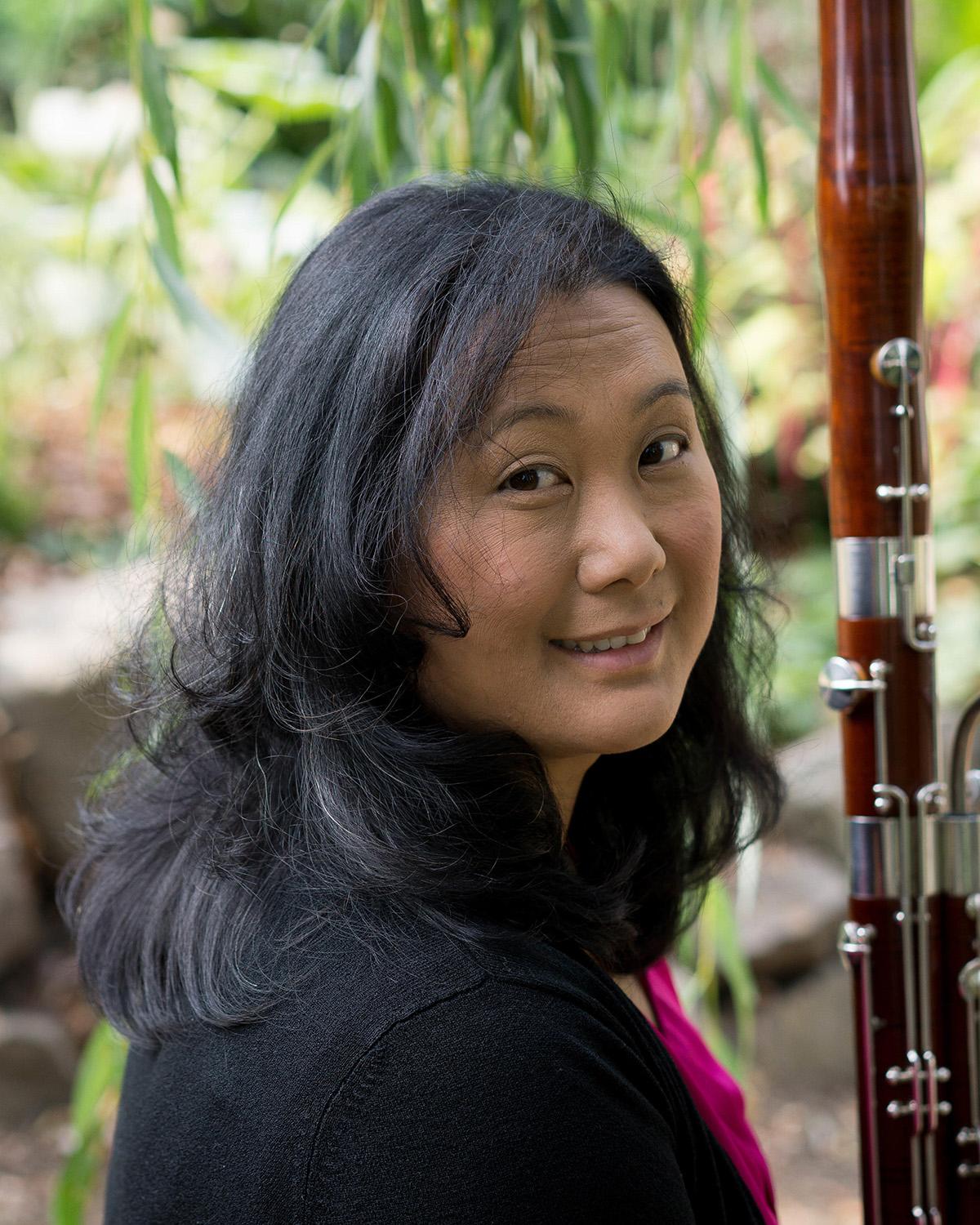 Elaine holding a bassoon, looking over her shoulder at the camera to smile