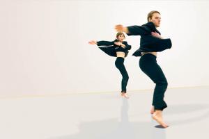 Two dancers in black clothing spin just above the floor