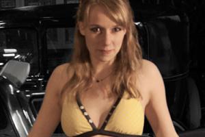 Photo of the show's main character, wearing a bikini top, looking at the camera while leaning on a car
