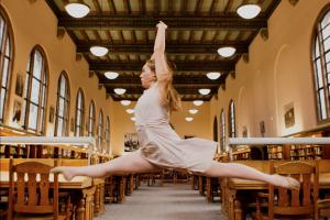 a dancer leaps between tables in an old fashioned library reading room