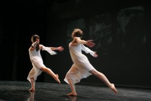 two dancers in white swooping leftward on black stage