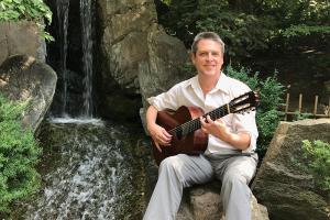 Paul Grove seated in natural setting with guitar