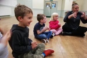 Deb Currier sits on the floor with small children learning a theatre exercise
