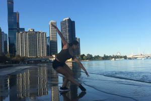 a dancer poses on a wet sand beach with skyscrapers behind