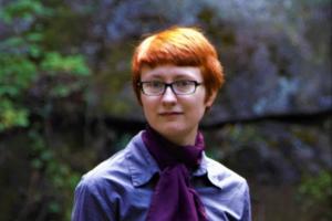 young person with short red hair and a dapper purple shirt and scarf