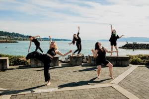 5 dancers, 3 on cement blocks and 2 on ground, in different artistic poses. A view of the bay behind them.