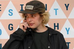 a young person with a black ball cap talks on an older style phone with a corded handset