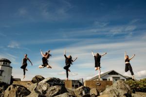 Five dancers leaping in the sky above a rocky terrain, each in a different artistic pose