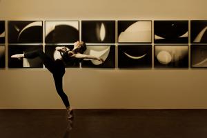A dancer makes a dramatic movement which matches the shapes of images portrayed on the wall behind