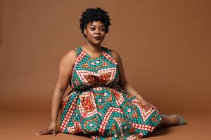 Rashawn Nadine Scott seated on the floor in a patterned dress looks confident and comfortable