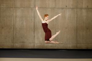 a dancer in a burgundy dress leaping in front of a concrete wall