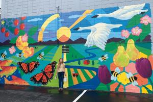 a person stands in front of a very large colorful mural on an exterior building wall
