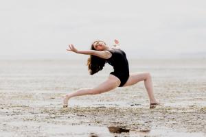 a dancer on the beach in a black leotard in a low lunge with arms outstretched