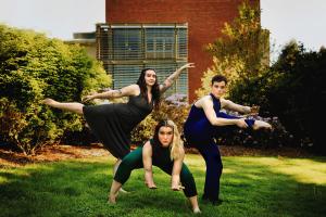 3 dancers in athletic poses in an evening-lit garden. One squatting, the others stand with a foot pointed outward.