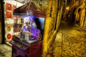 a glass enclosed kiosk with a purple fortune teller sits at the end of a twilit alley in Lyon France