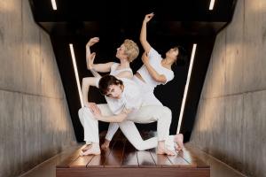 three dancers in white strike angular poses in a concrete hall