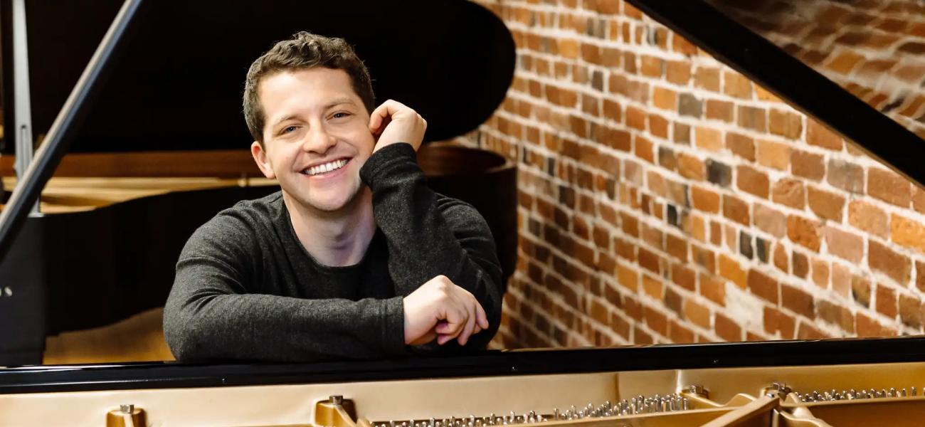 Henry Kramer leaning on an open Steinway piano with a big relaxed smile