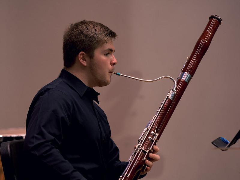 Bassoon player looks at a music stand in front of him as he performs with calm focus.