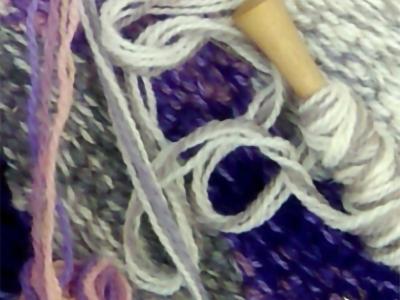 detail of loose yarn and the end of a yarn-wrapped knitting needle resting on a knitted background