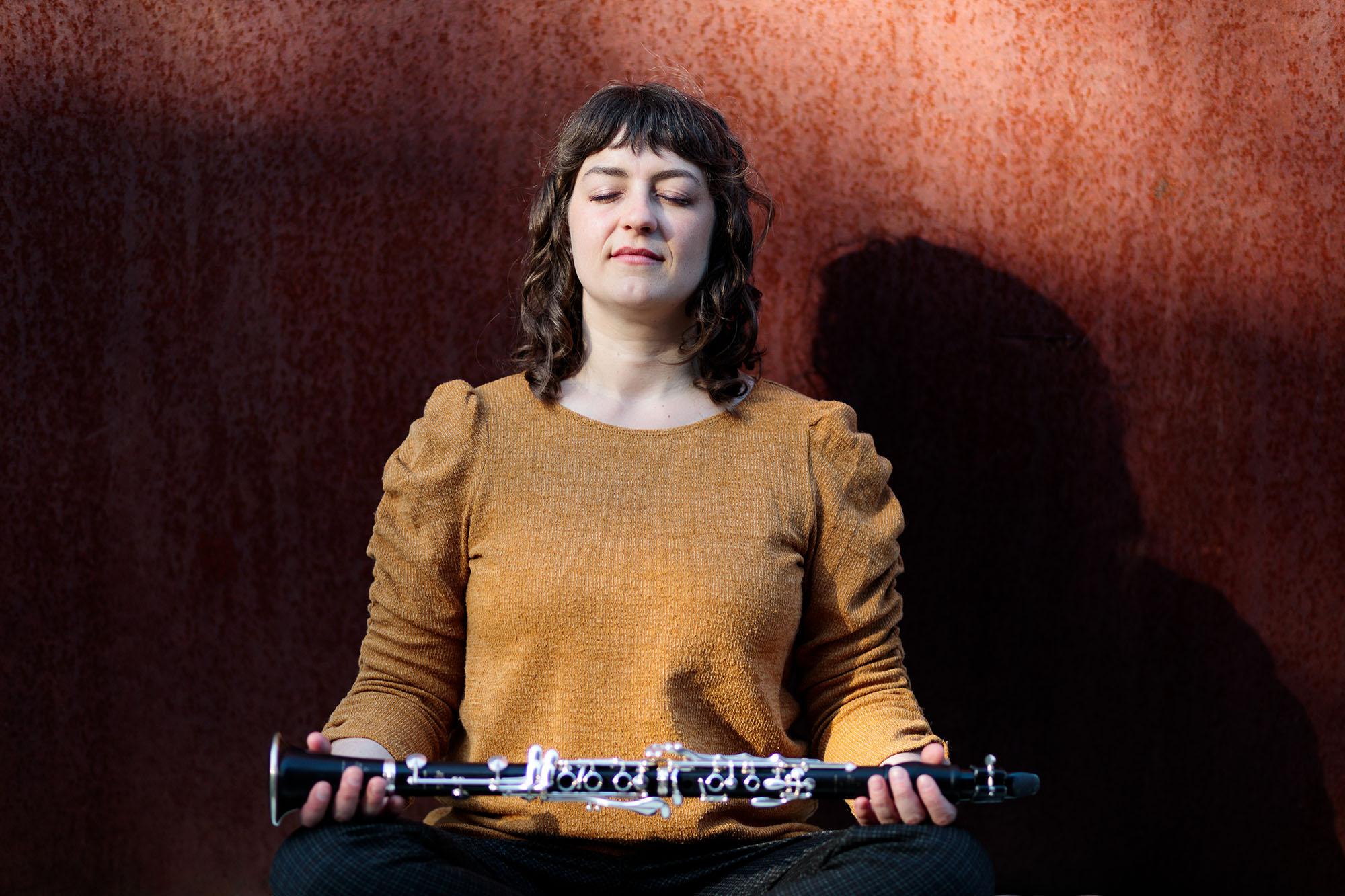 Rachel Yoder assumes a meditative pose with eyes closed, holding a clarinet horizontally across both open palms