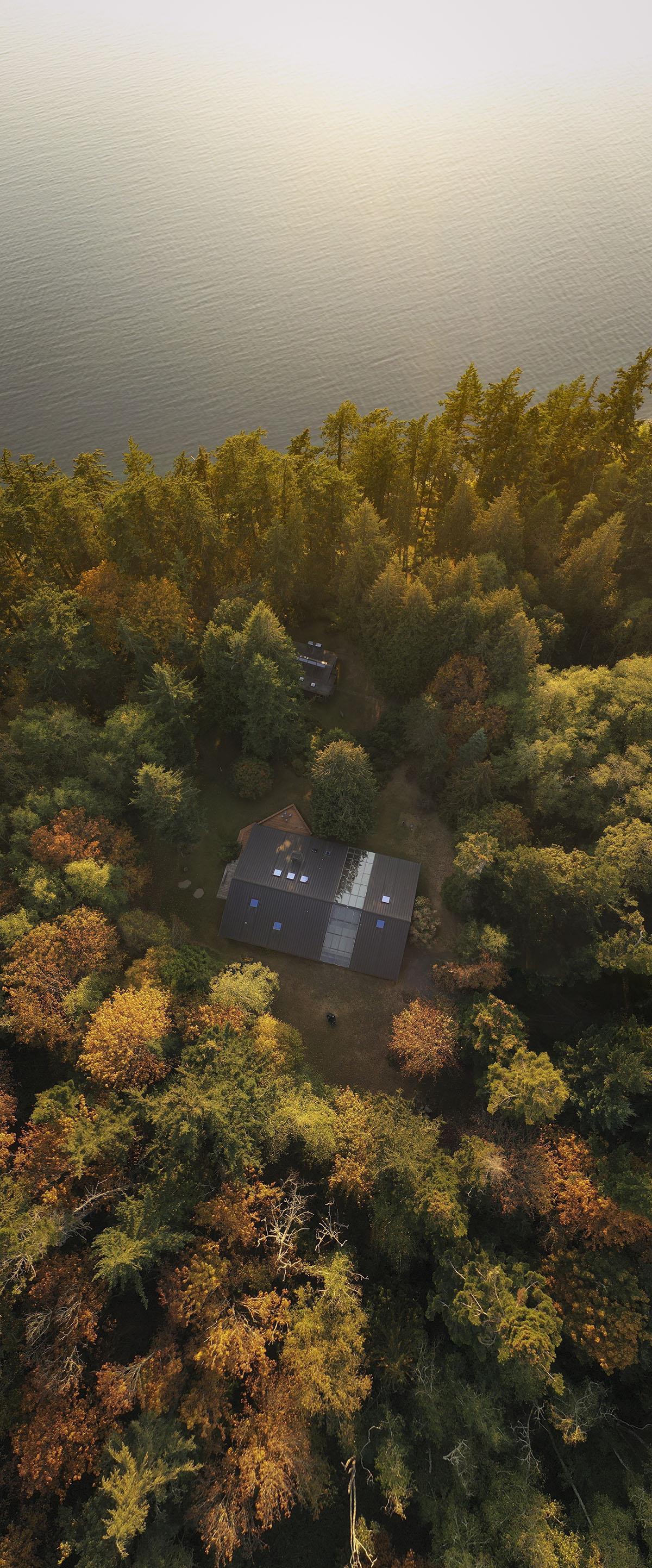 arial view of a small building surrounded by trees very close to a shining body of water
