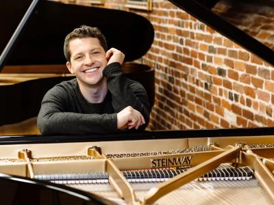 Henry Kramer leaning on an open Steinway piano with a big relaxed smile