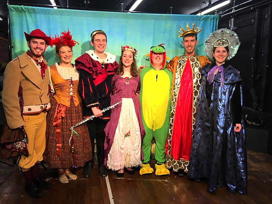 six performers in bright, fanciful costumes, including one dressed like a dragon.
