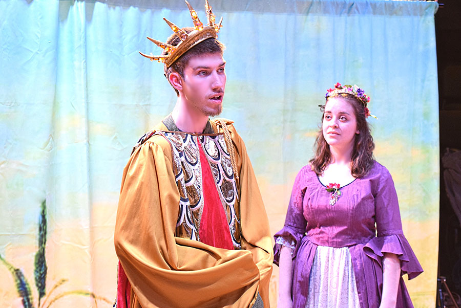 actor with crown orates while actor in purple dress attends