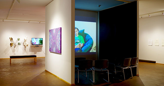 On the left, small paintings, then a wall, on the right, a video installation in a dark space