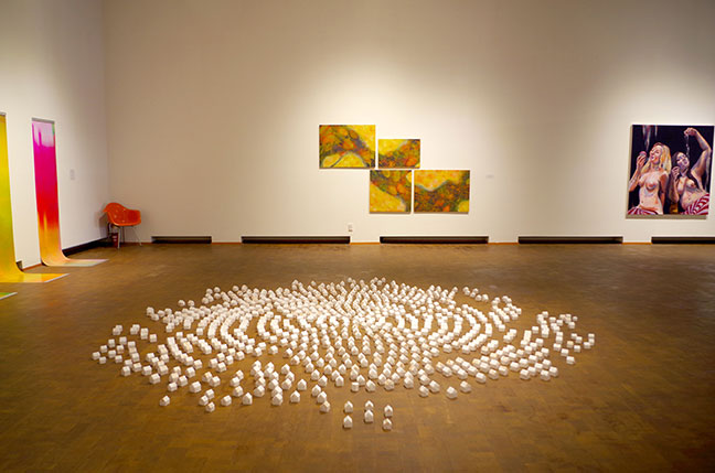 Gallery walls are visible. In foreground, a collection of very small sculptures in a circular pattern.