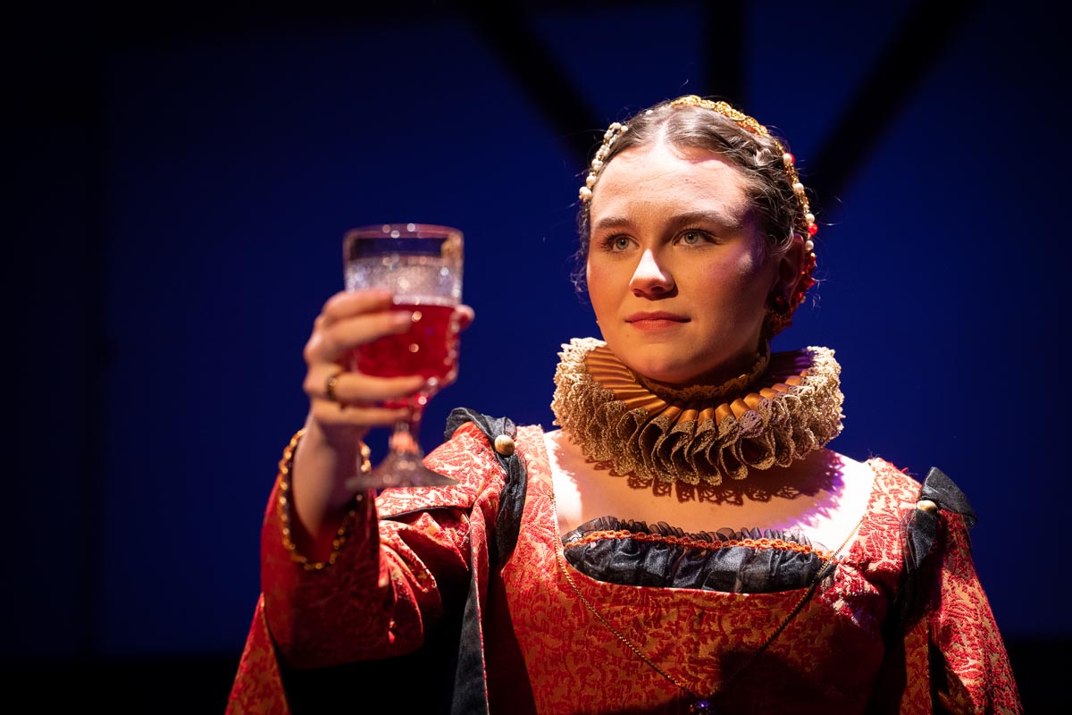 A person in a ruffed collar holds aloft a glass of port