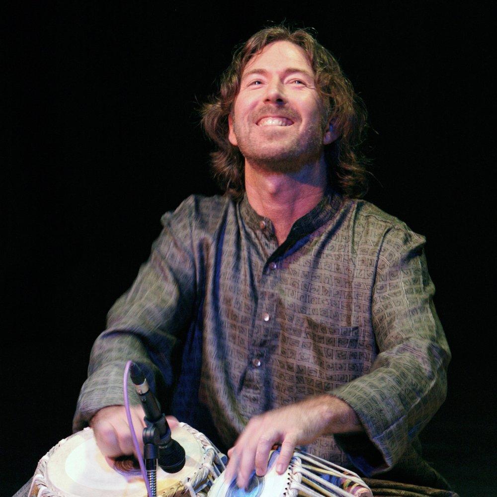 Ty Burhoe looks up with a joyful smile while playing the tabla - a kind of drum. 